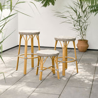 Gold metal bar stools with woven grey and white patterned seats, set against a natural green backdrop.