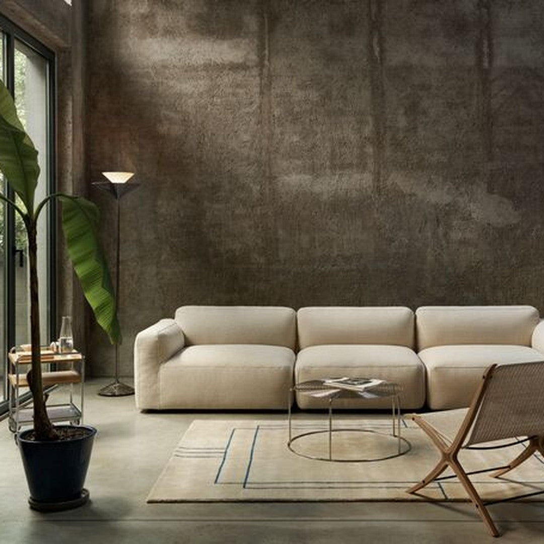 Cream-colored sectional sofa, geometric blue lines on a beige rug, set against a textured gray wall.