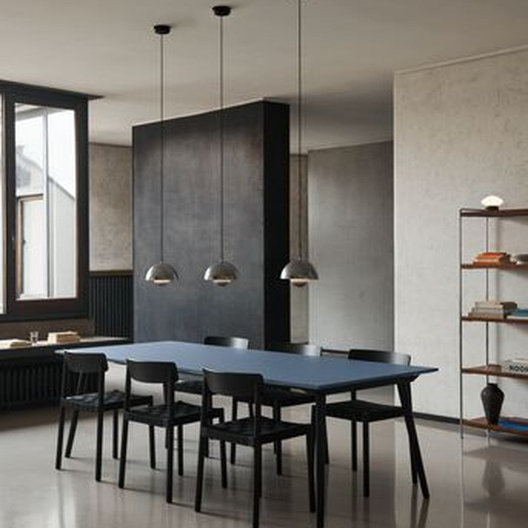 Modern dining room featuring a deep blue table, black chairs, and gray walls, with metallic pendant lighting above.