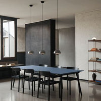 Modern dining room featuring a deep blue table, black chairs, and gray walls, with metallic pendant lighting above.