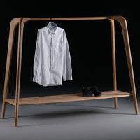 White button-up shirt on a minimalist natural wood clothing rack with a sleek black base and stylish black shoes.