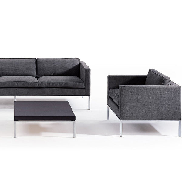 Modern gray sofa and armchair with a sleek black coffee table, featuring a minimalist design and subtle patterns.