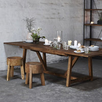 Rustic wooden dining table and stools with natural tones, complemented by clear glassware and white candles.