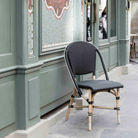 Black woven chair with bamboo legs against a muted green wall and patterned tile backdrop. Stylish outdoor decor.