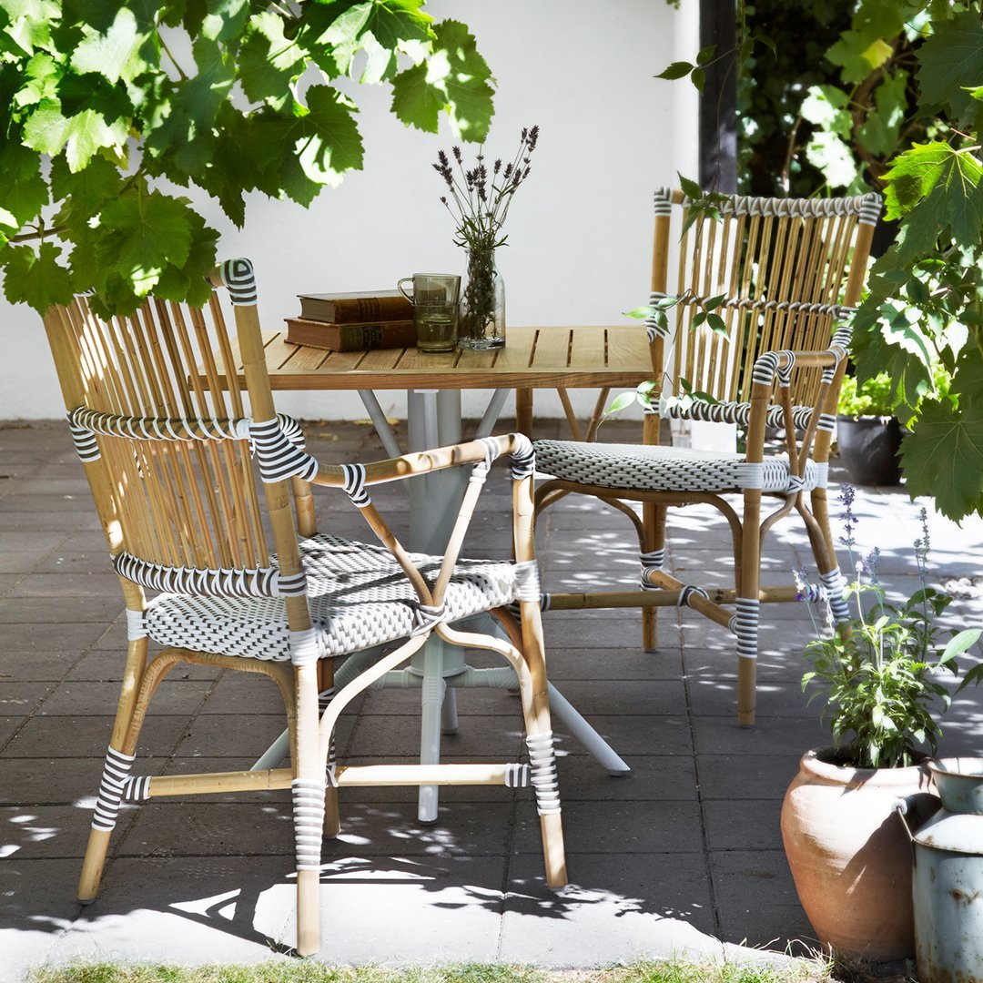 "Natural bamboo chairs with black and white striped cushions, set against a lush green backdrop."