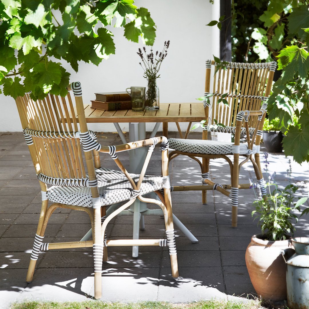 "Natural bamboo chairs with black and white striped cushions, set against a lush green backdrop."