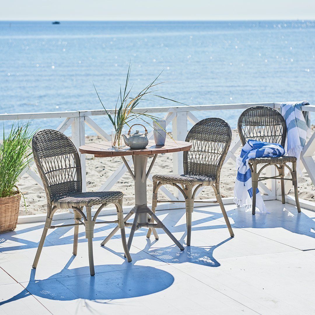 "Outdoor dining set featuring gray wicker chairs and a wooden table against a beach backdrop."
