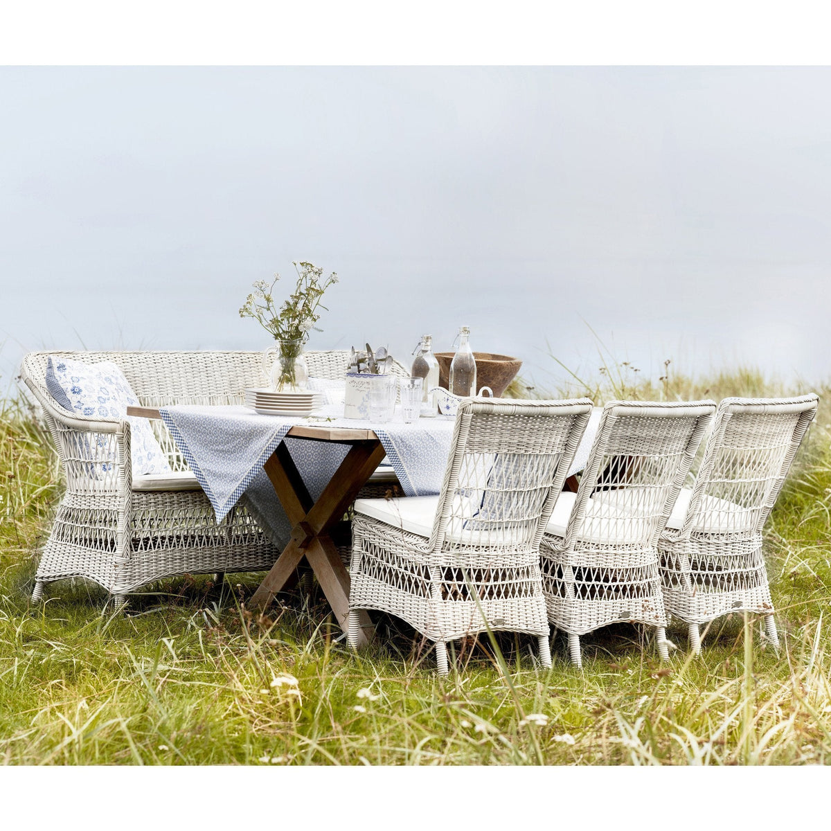 White wicker dining set with natural wood accents, featuring a simple, elegant design against a soft green backdrop.