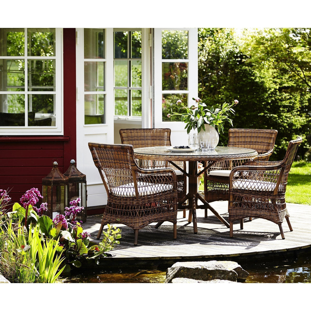 "Four rattan patio chairs with a round table, featuring natural hues and striped cushions, set on a wooden deck."
