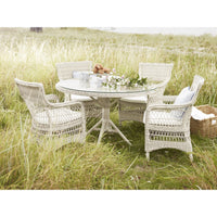 Round white wicker dining table with matching chairs, featuring a natural, textured pattern in a grassy outdoor setting.