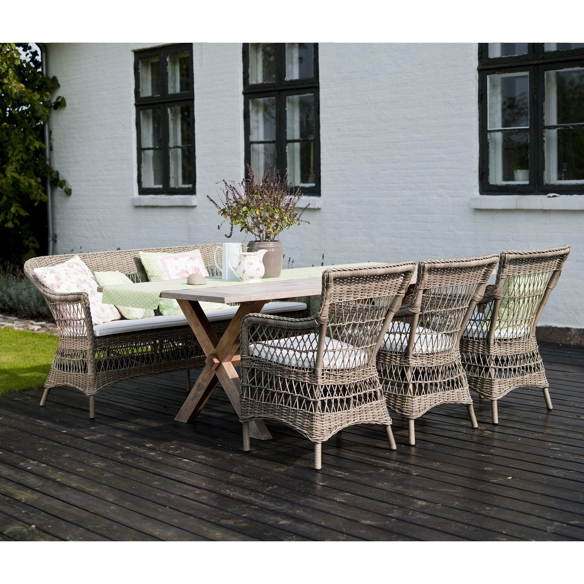 "Neutral wicker patio dining set with soft green cushions against a rustic wood deck."
