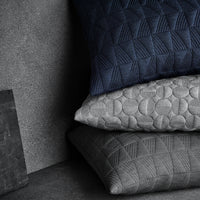 Stack of three decorative pillows in navy blue, light gray, and dark gray with textured geometric patterns.