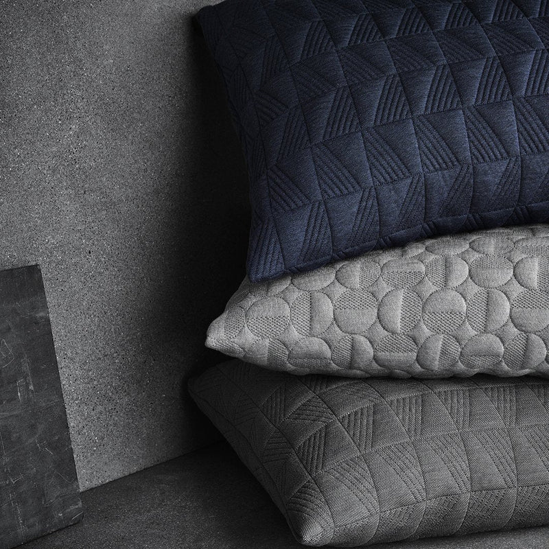 Textured pillows in navy, light gray, and dark gray, featuring geometric and circular patterns on a muted background.