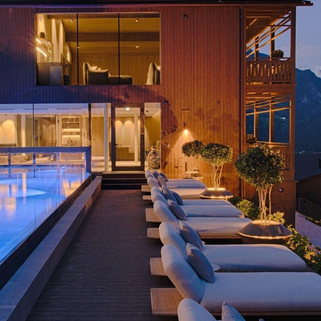 Elegant outdoor lounge with neutral cushions, wooden accents, and soft blue pool lighting under a twilight sky.