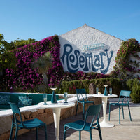 Vibrant purple bougainvillea against a white wall, with teal chairs and turquoise cushions, creating a lively outdoor setting.