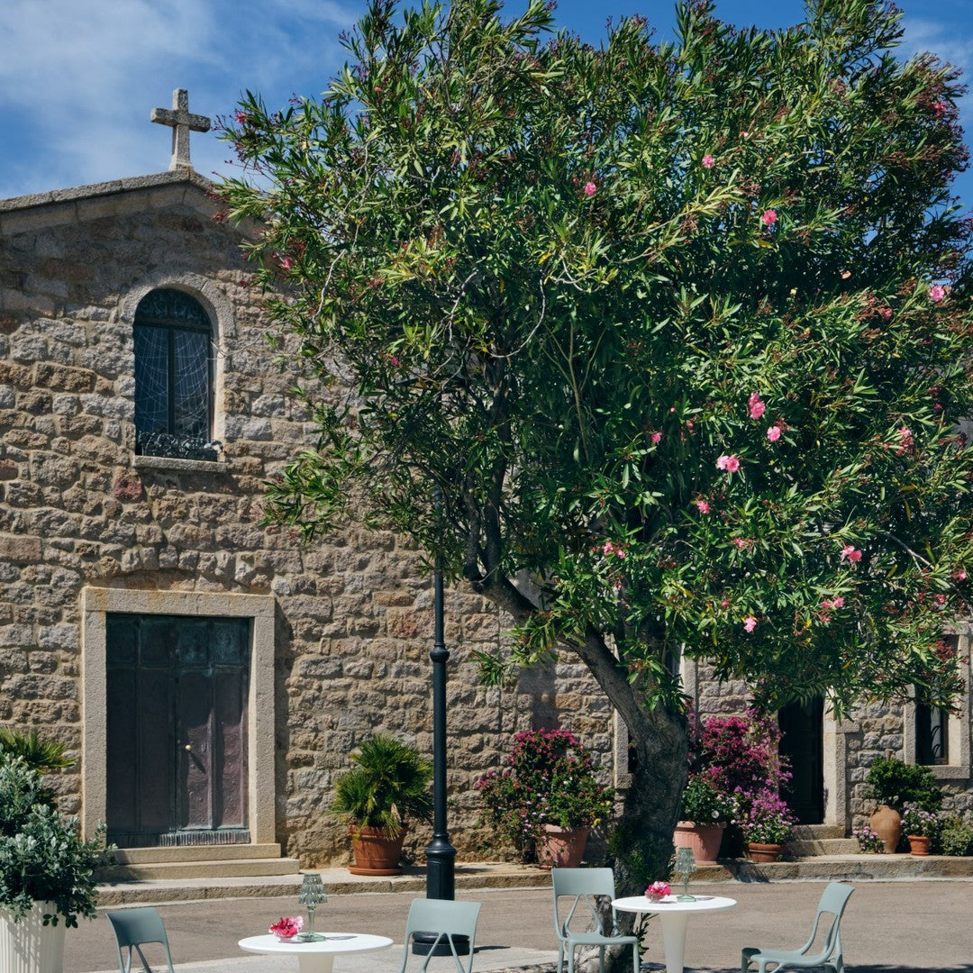Stone facade with green foliage and pink flowers against a blue sky, creating a vibrant outdoor scene.