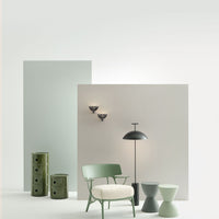 "Pastel green and muted gray backdrop with black lighting fixtures and soft white chair, highlighting modern decor."