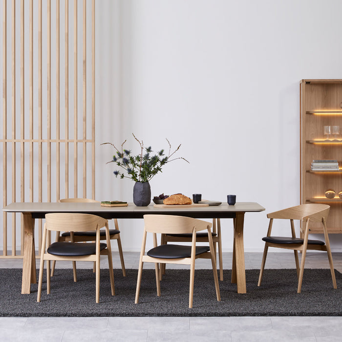 Modern wooden dining table with natural wood finish, black cushioned chairs, and minimalist gray rug. Elegant decor.