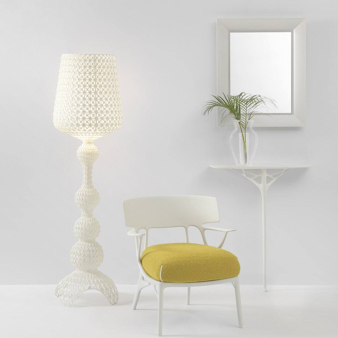 White woven lamp, yellow cushion chair, and a clear vase on a white table in a modern, minimalist setting.
