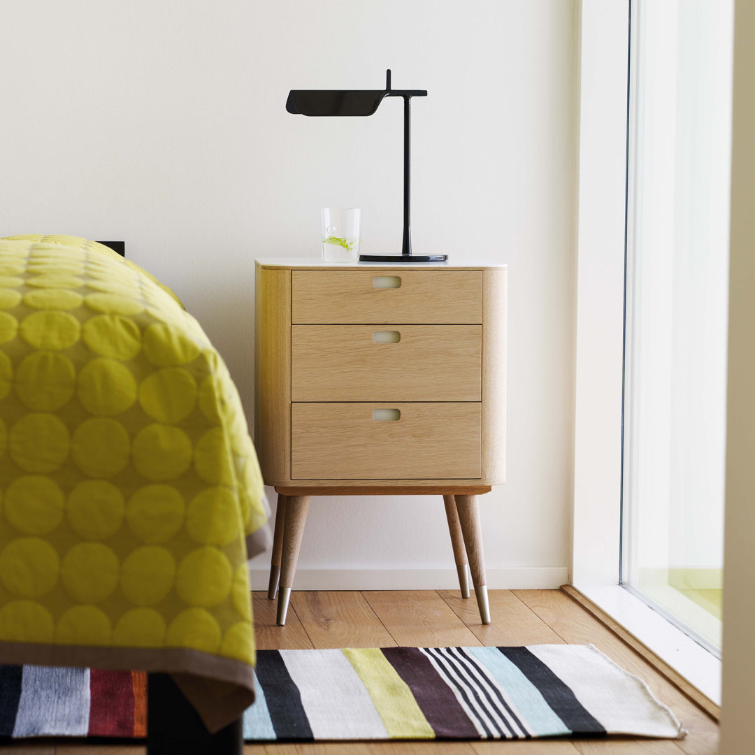 Yellow circular patterned bedding, a natural wooden nightstand, and a striped multicolor rug complement a modern bedroom.