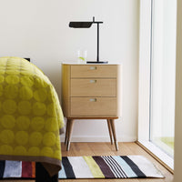 Yellow circular patterned bedding, a natural wooden nightstand, and a striped multicolor rug complement a modern bedroom.
