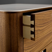 Close-up of rich walnut wood grain with a smooth white surface and polished gold accents on a drawer detail.
