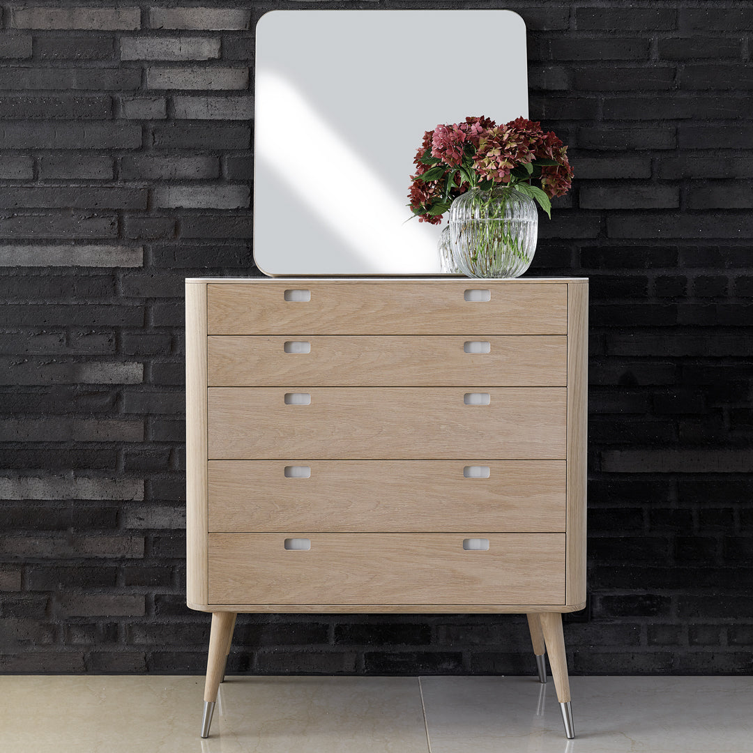 Light oak dresser with a minimalist design, featuring smooth lines and silver accents against a dark stone wall.