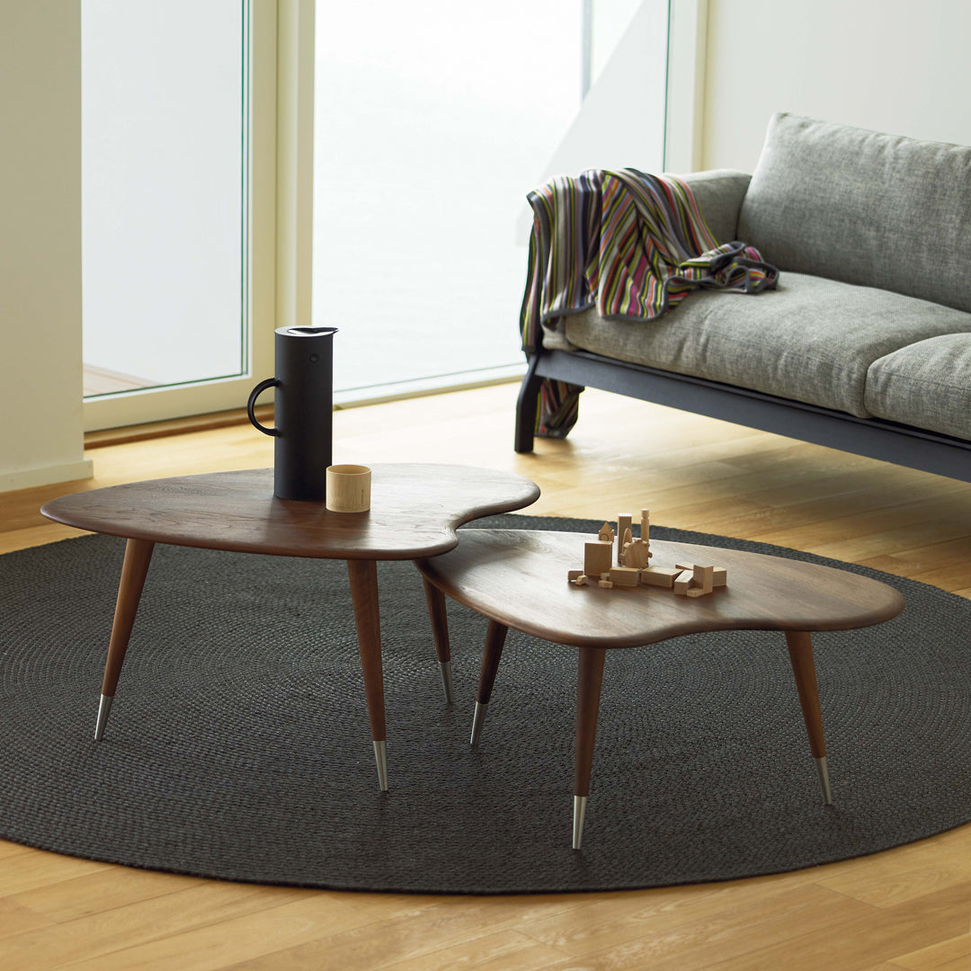 Wooden coffee tables in organic shapes on a dark gray rug, complementing a light-filled, modern living space.
