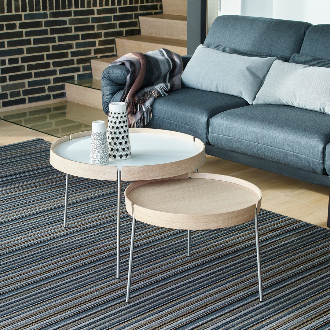 Modern round coffee tables with natural wood finish and sleek metal legs, set on a multicolored striped rug.