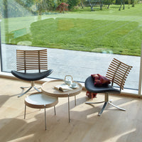 Two modern lounge chairs with wood slats and black seats, paired with a round coffee table in a bright, natural setting.