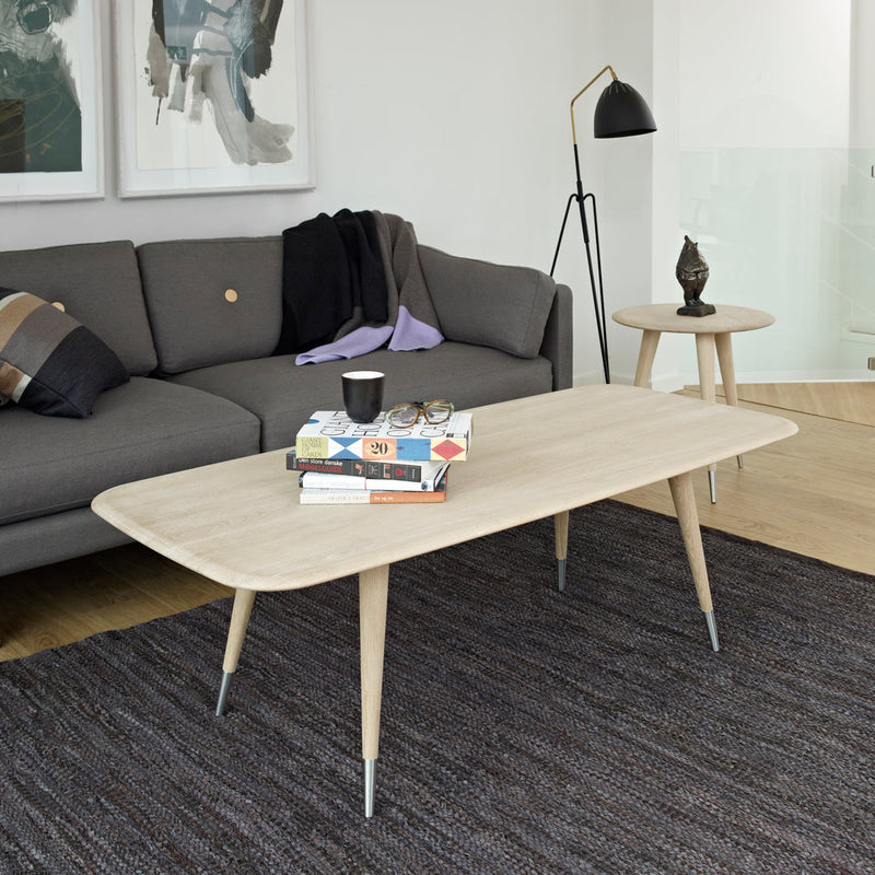 Light wood coffee table with tapered legs, set against a dark woven rug and complemented by gray sofa and decor.