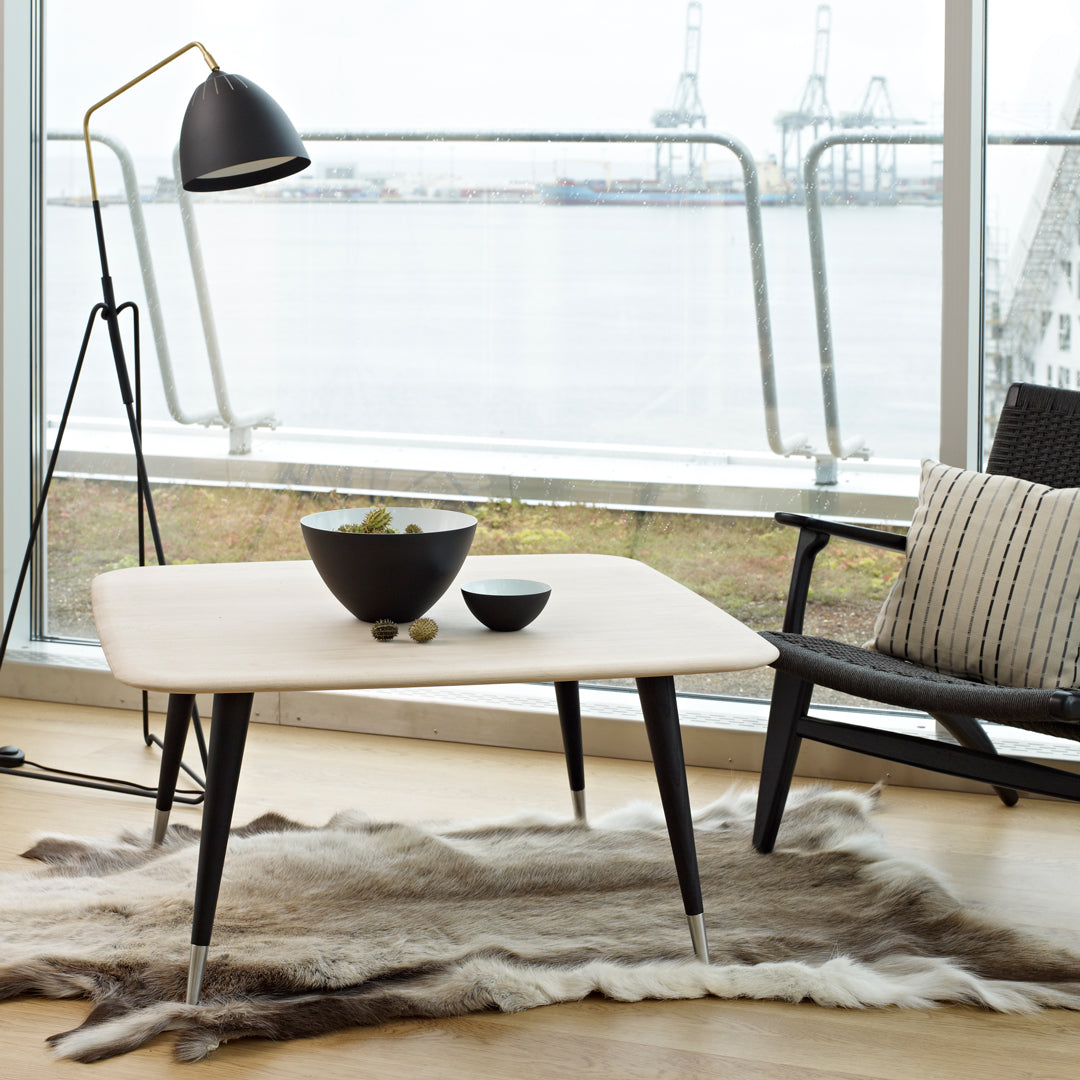 "Modern light-colored coffee table with sleek black legs and a minimalist design, paired with a plush fur rug."