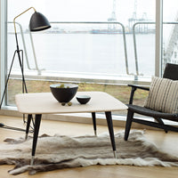 "Modern light-colored coffee table with sleek black legs and a minimalist design, paired with a plush fur rug."