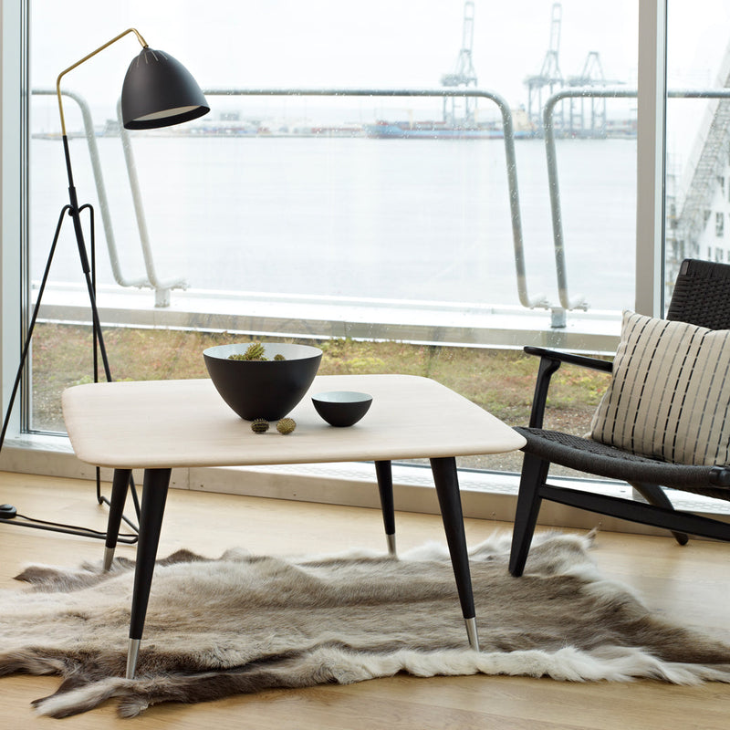 "Modern light-colored coffee table with sleek black legs and a minimalist design, paired with a plush fur rug."