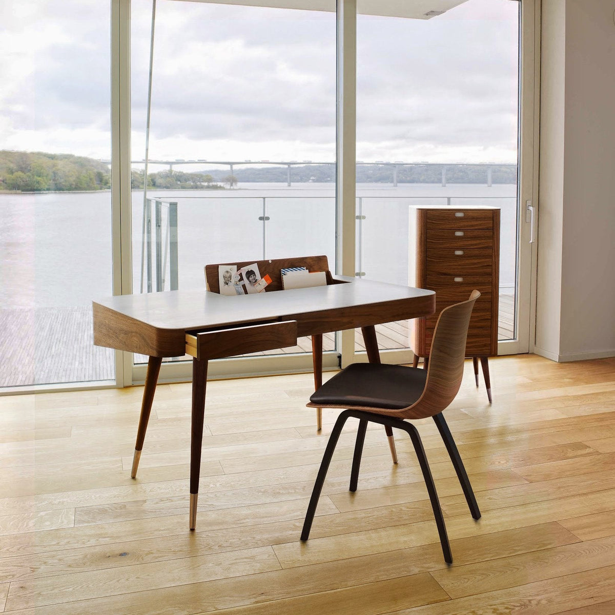 Mid-century modern desk with rich walnut finish, sleek white top, and a contrasting black chair against a serene natural backdrop.