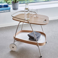Wooden serving cart with light oak finish, white shelf, and stainless steel accents, featuring a sleek, minimalist design.