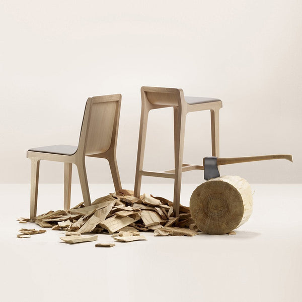 Two minimalist wooden chairs in muted beige, surrounded by wood shavings against a neutral background.