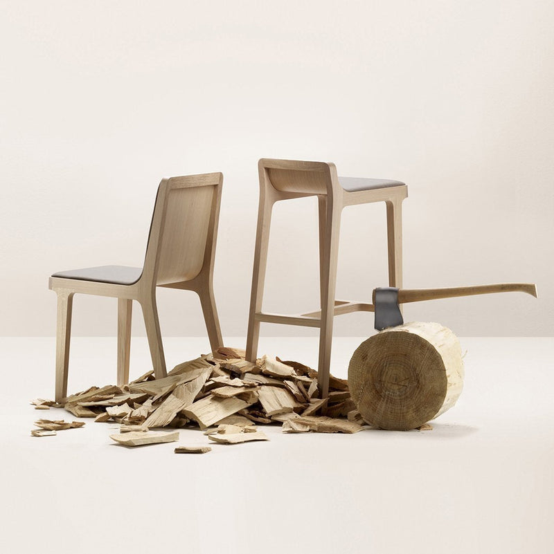 Two minimalist wooden chairs in muted beige, surrounded by wood shavings against a neutral background.