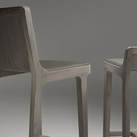 Two minimalist chairs in soft gray wood with subtle grain patterns, featuring sleek, modern lines.