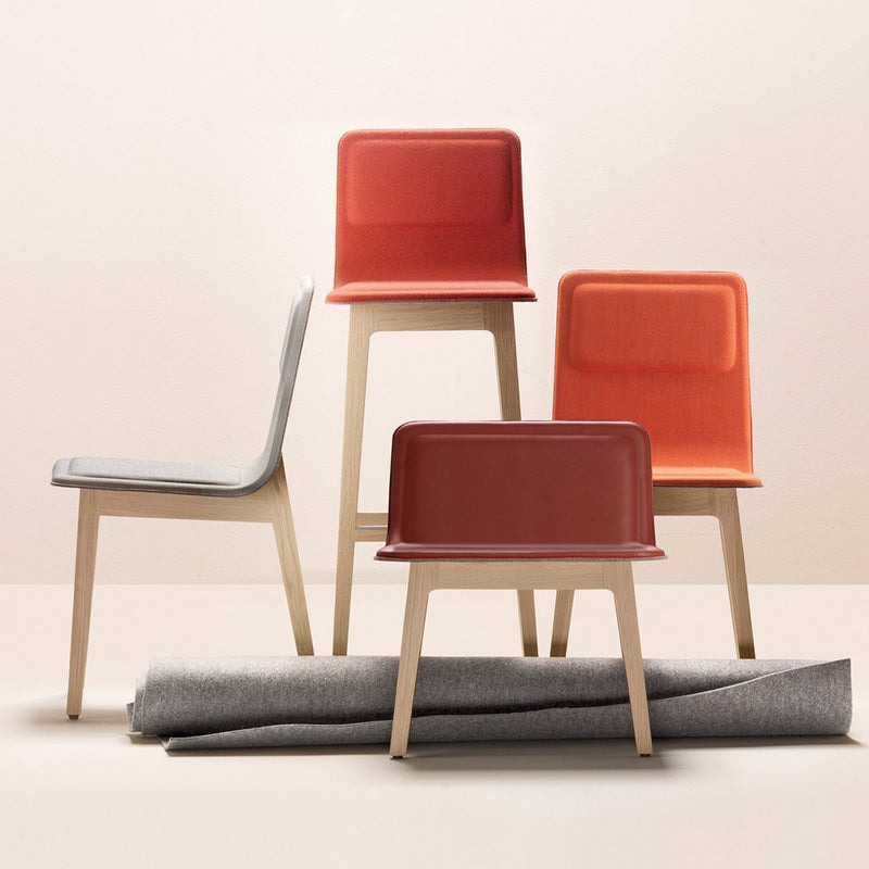 Colorful modern chairs in red, orange, and gray with wooden legs, complemented by a soft gray fabric roll.
