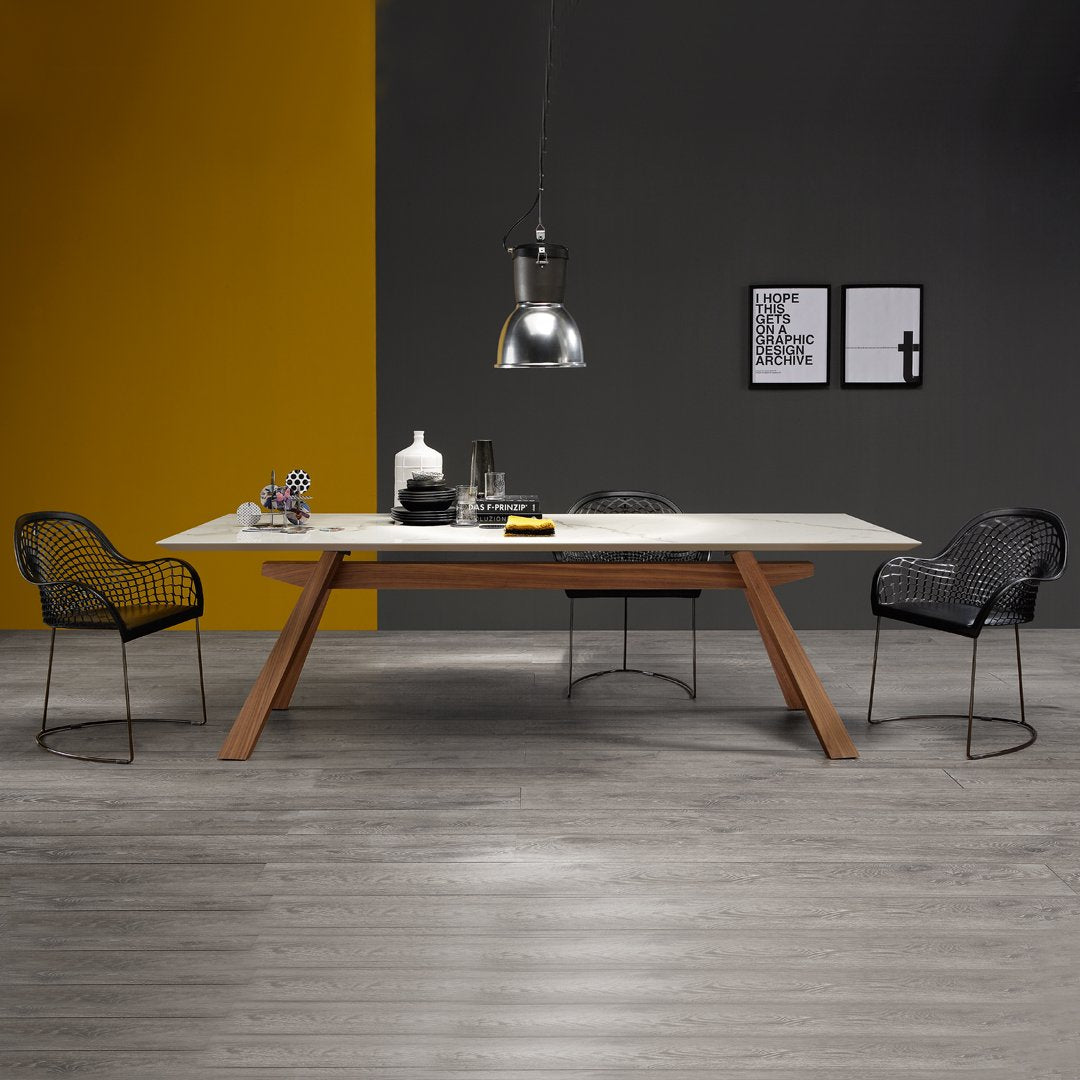 Modern dining table with a white surface, wooden legs, gray walls, and yellow accent wall. Black wire chairs add contrast.