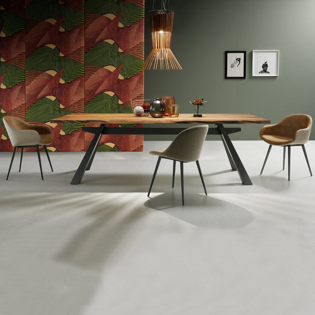 Modern dining table with a natural wood finish, complemented by beige and brown chairs against a colorful patterned wall.
