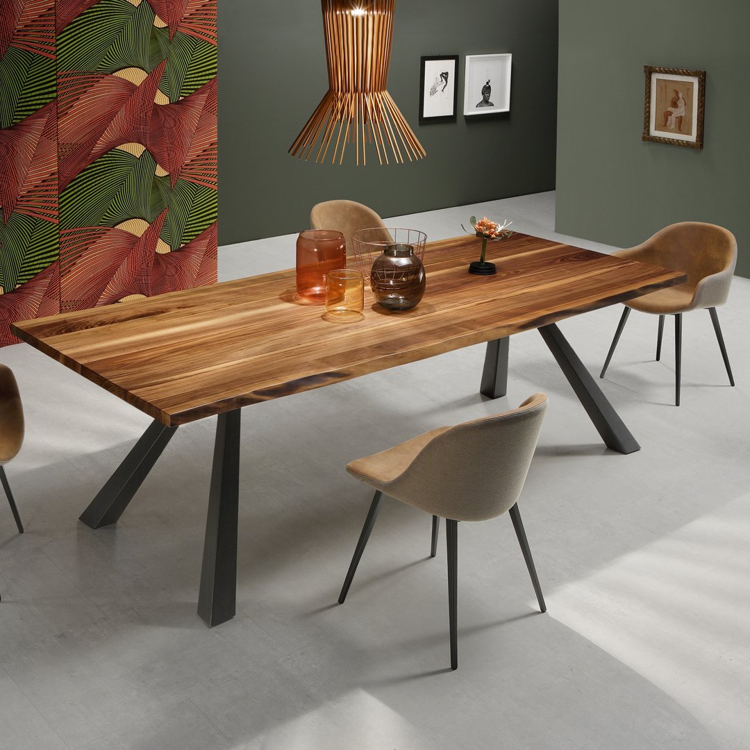 Wooden dining table with natural tones, paired with beige chairs and a green accent wall featuring colorful leaf patterns.