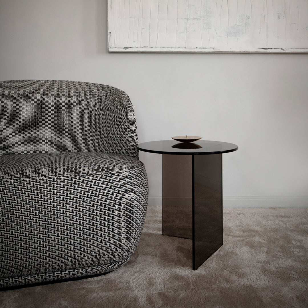 Textured gray fabric sofa beside a sleek black glass side table on a soft beige carpet, creating a modern, sophisticated look.
