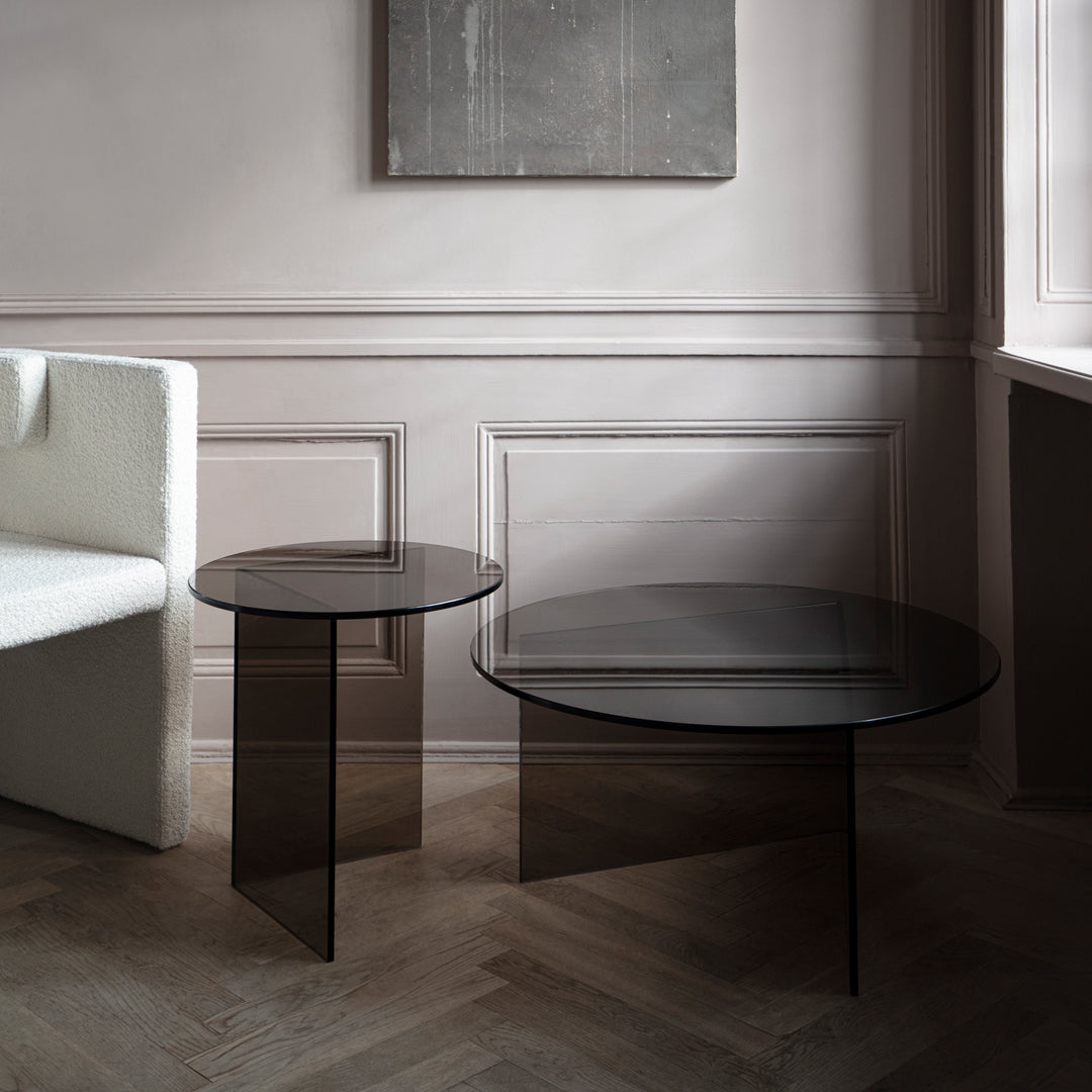 Black glass coffee tables with sleek, minimalist designs, set against a soft, neutral-toned interior.