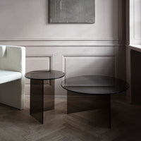 Black round glass coffee tables with sleek designs, set against a light-colored wall and wooden floor.