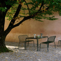 Green metal outdoor dining set with mesh pattern against a warm, muted beige wall and natural surroundings.