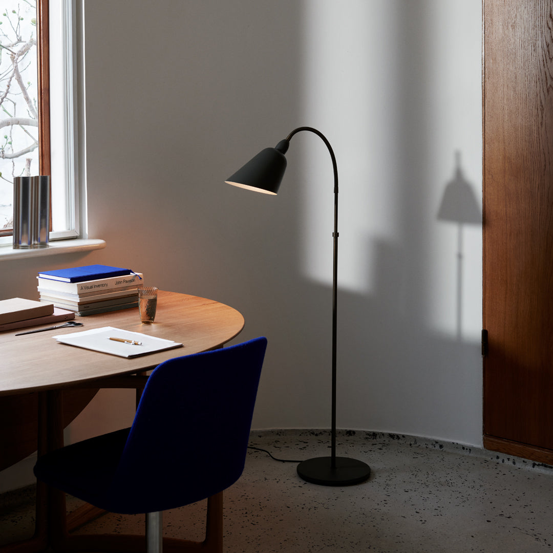 Black floor lamp with a sleek, curved design, casting a shadow on a light gray wall, complemented by a blue chair.