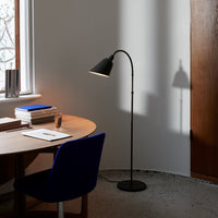 Black floor lamp with a sleek, curved design, casting a shadow on a light gray wall, complemented by a blue chair.