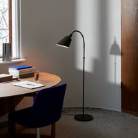 "Black floor lamp with a sleek curved design, casting a soft shadow on a light gray wall."